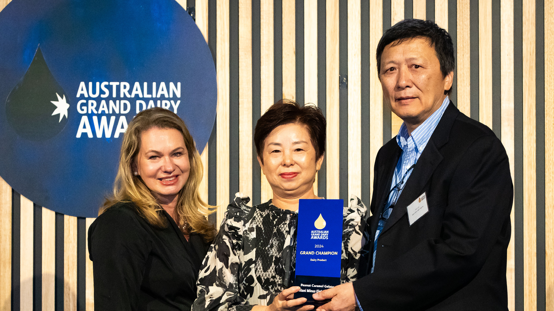 A sponsor and two award winners pose with an AGDA trophy.