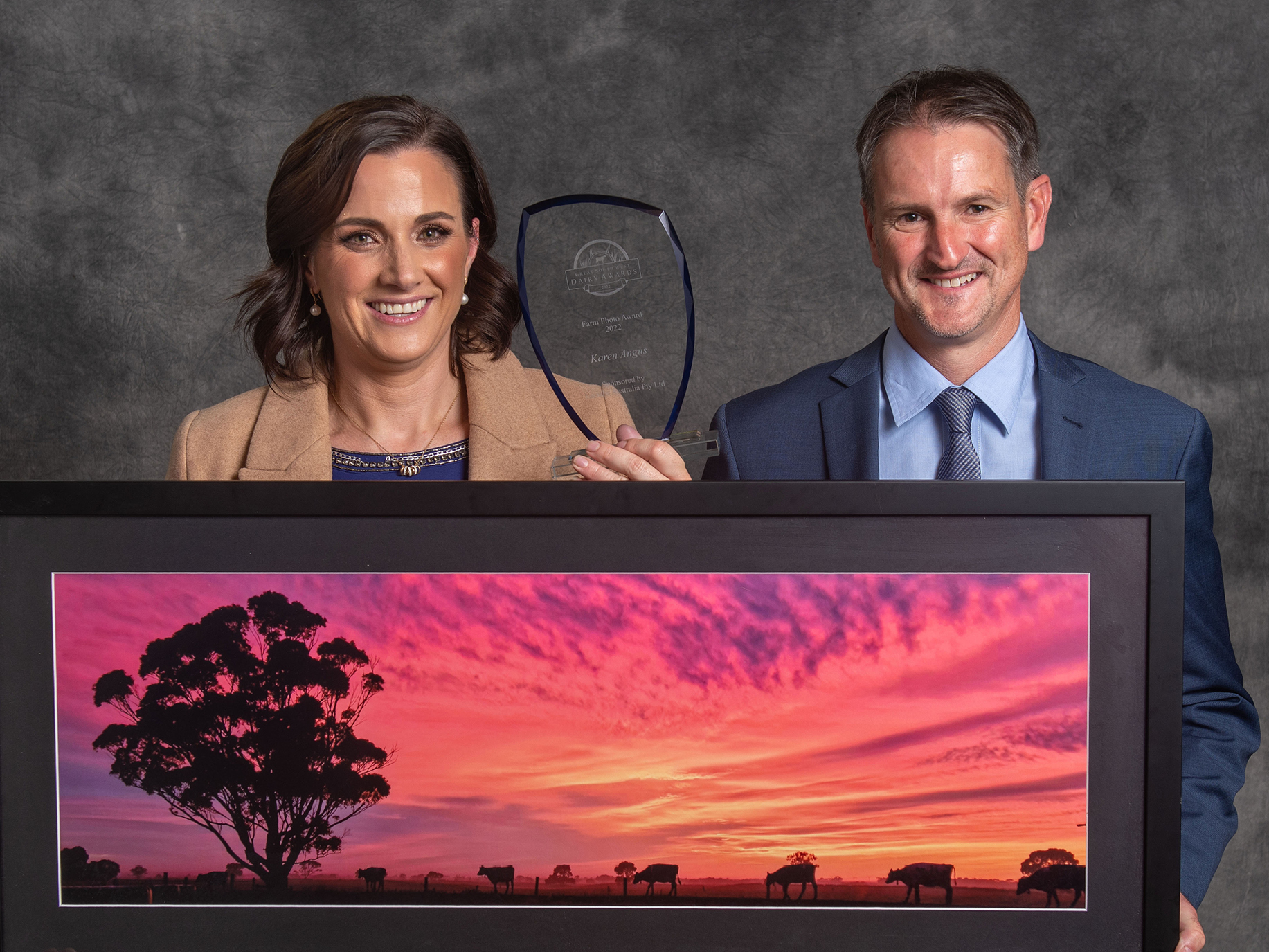 Two award recipients are posing with their award trophy and a large framed photo.